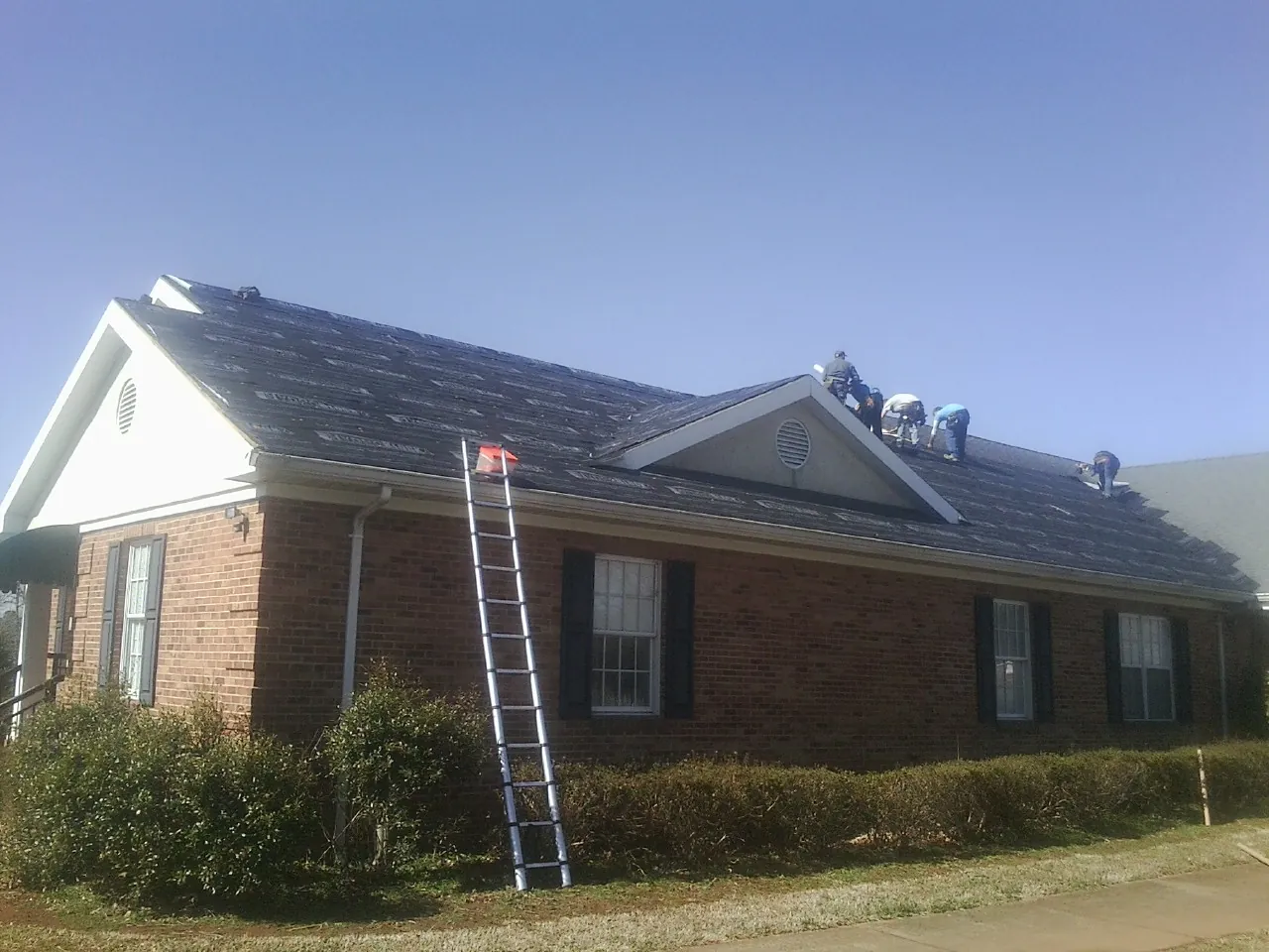 Crew tearing shingles off a brick ranch roof with a ladder set — Emergency Roof Repair work by our crew in Elvaston