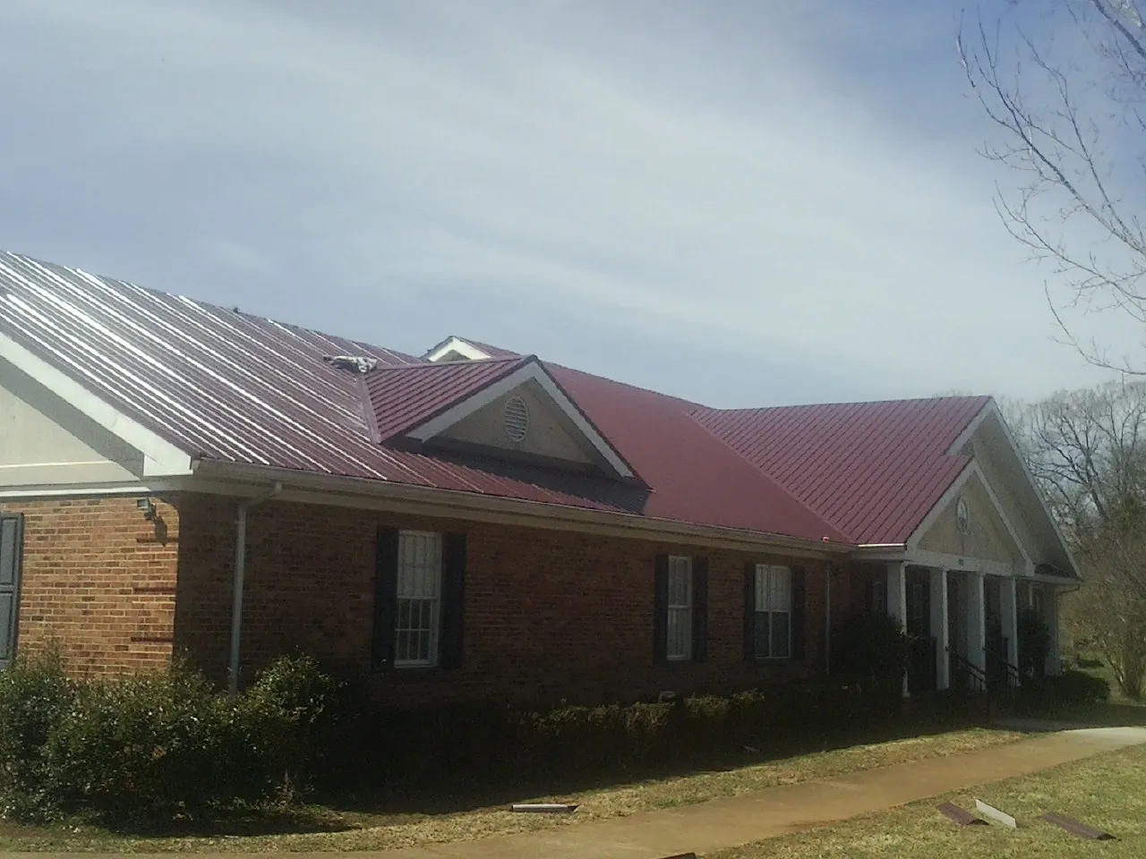 Red metal roof with gabled entries on a long brick building, from a Hail Damage Roof Repair job in Elvaston