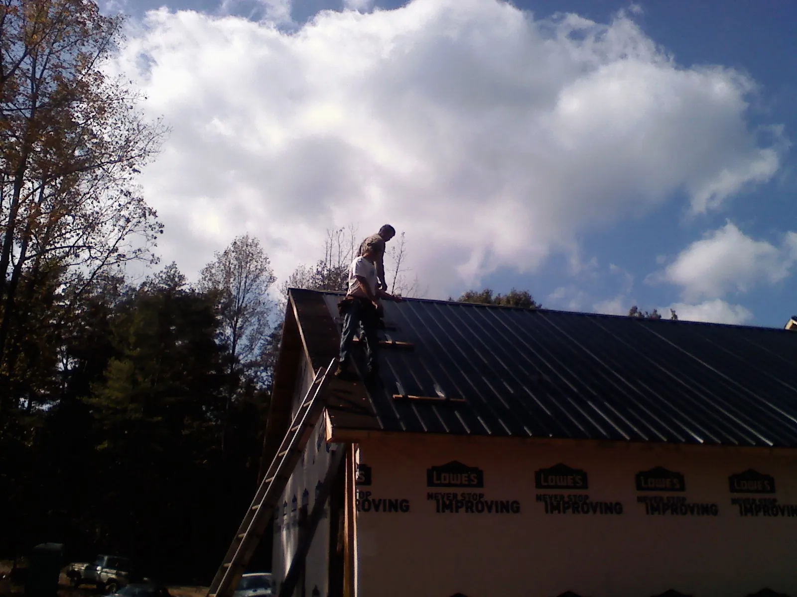 Roofer fastening dark metal panels high against a cloudy sky, from a Roof Inspection job in Elvaston