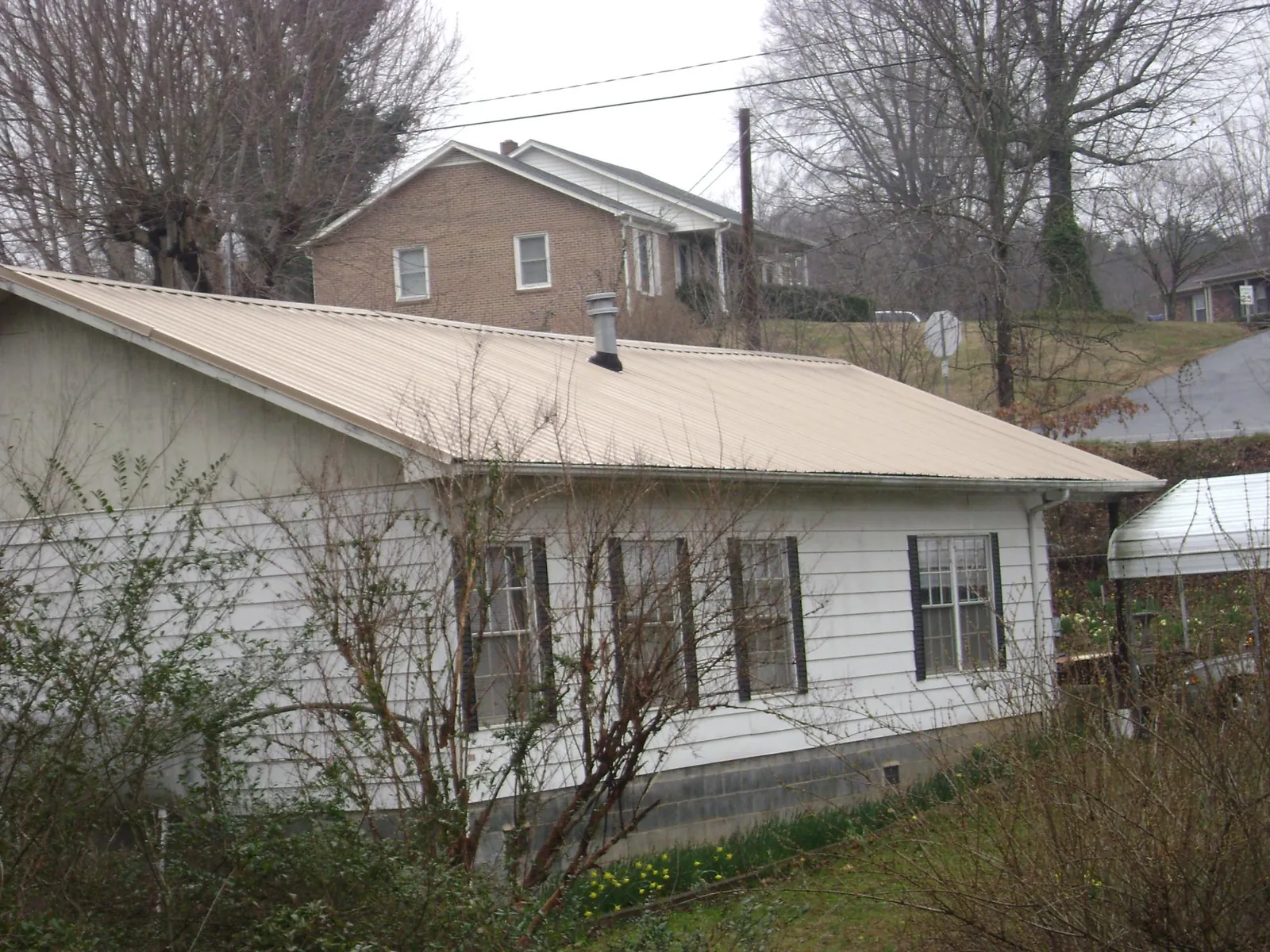 Tan metal roof on a white sided house set into a hillside — Commercial Roofing by Roofing Brothers in Elvaston