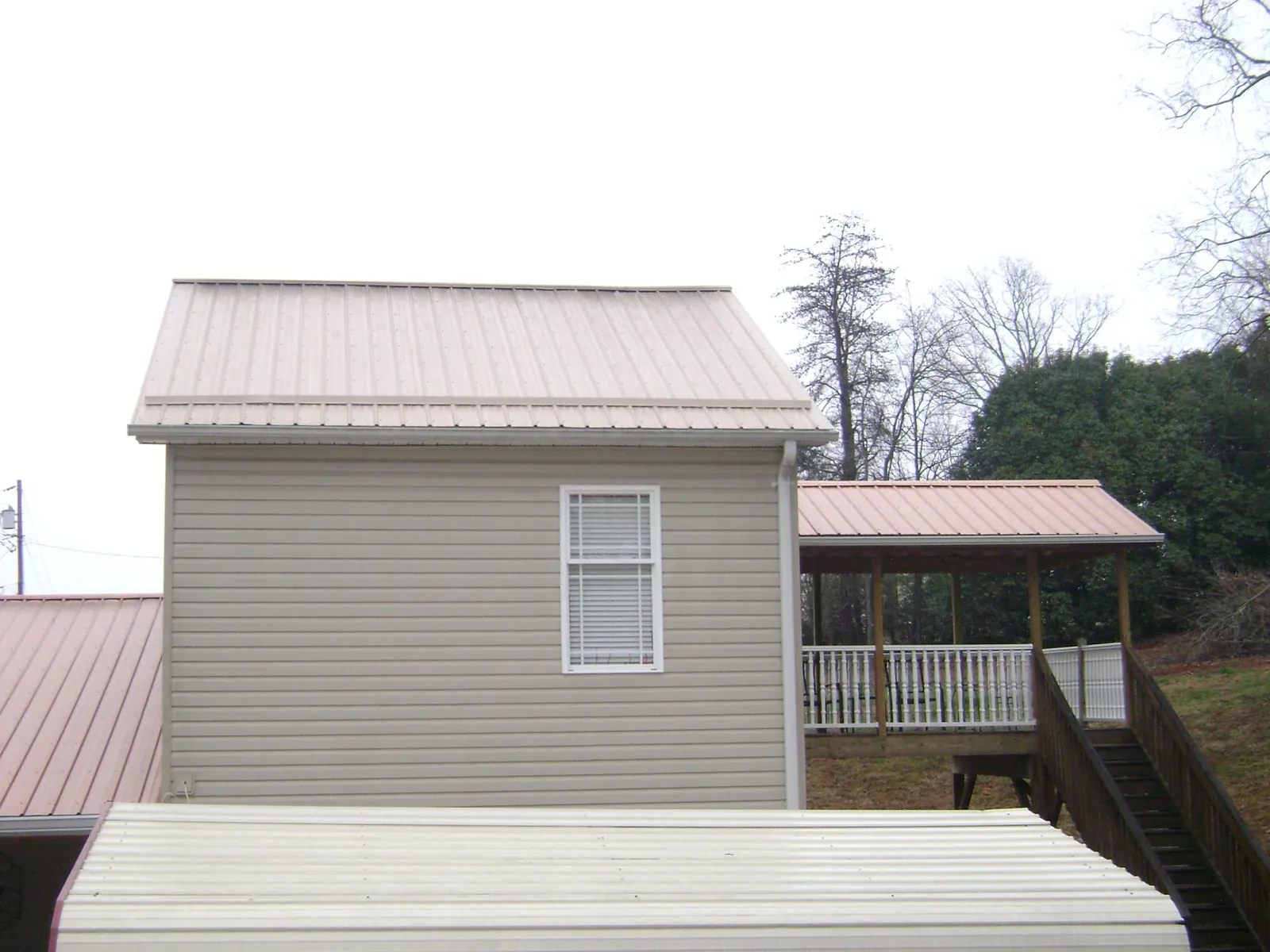 Tan metal roofs on a two story addition and attached porch, from a Roof Replacement job in Elvaston